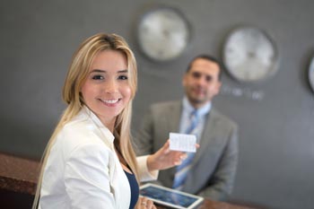 Frau an Hotelrezeption mit Rezeptionist im Hintergrund